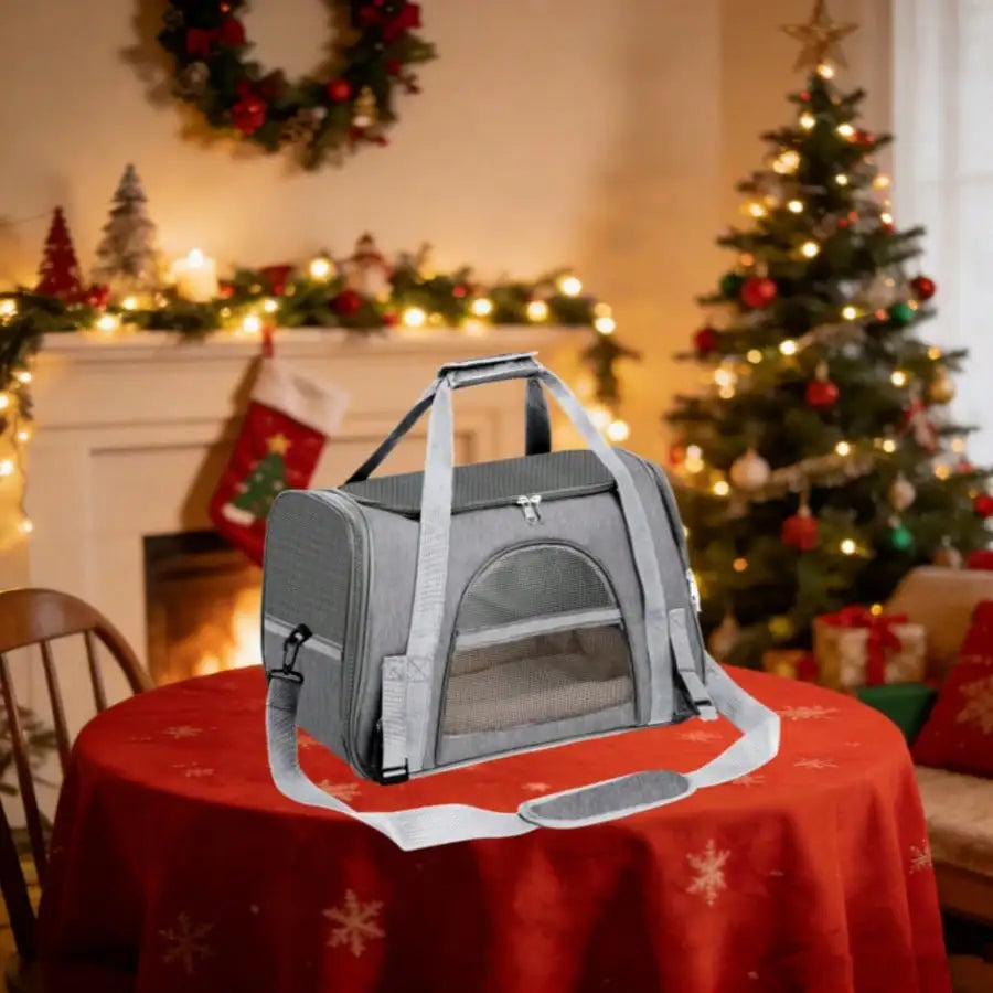 Grey pet carrier bag with mesh windows on a red tablecloth with Christmas decorations in the background